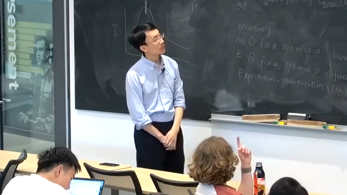 Pengtao Xie is pictured standing near a chalkboard filled with mathematical notes, addressing a classroom of attentive students.