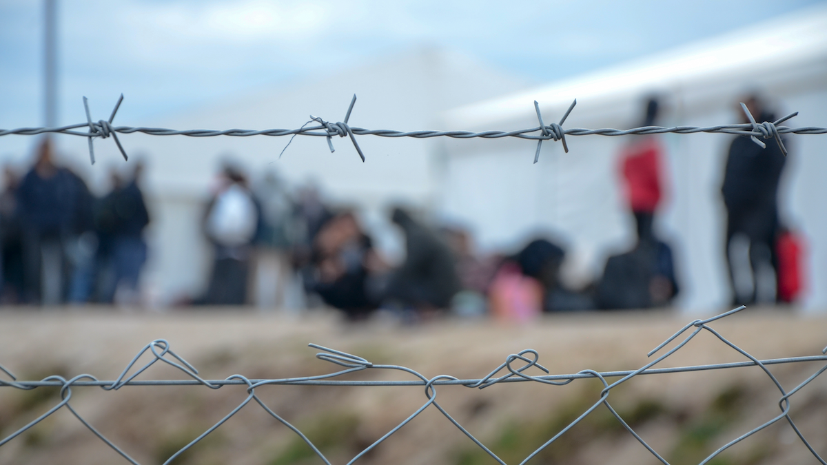 Migrants out of focus behind barbed wire fence